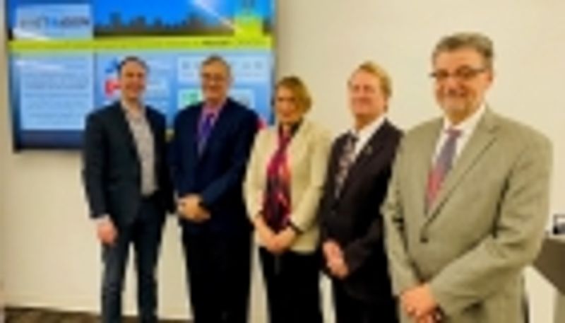 Blurry photo of five people posing against a television and cream-colored wall