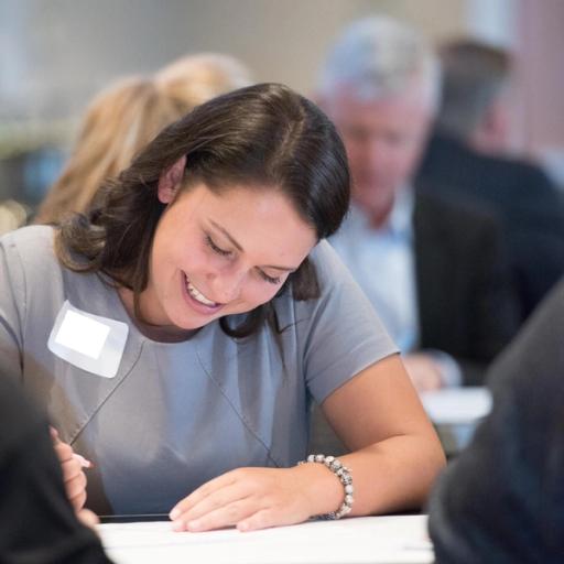 A woman wearing a bracelet smiles while writing something on a white table