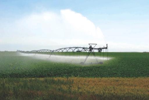 Farming machinery sprays a green field with water on a hot day.
