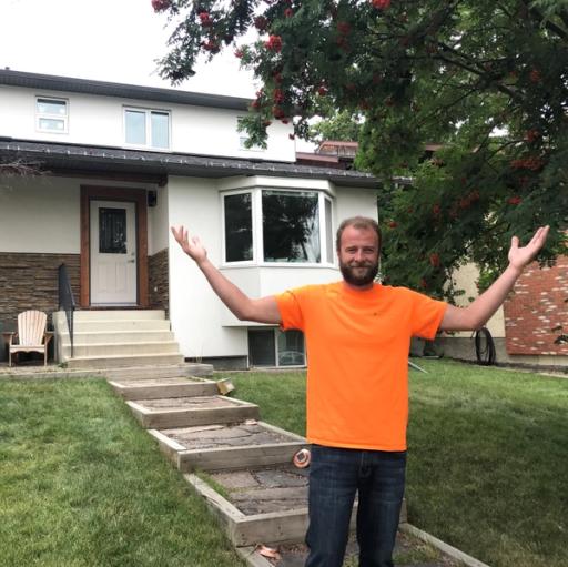 A man in an orange shirt stands with his arms spread wide in front of a white smart home