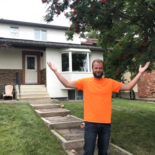 A man in an orange shirt stands with his arms spread wide in front of a white smart home