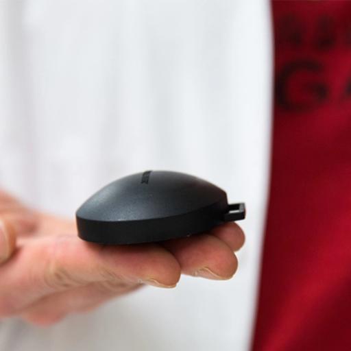 A person holes a black device in front of them against a white backdrop