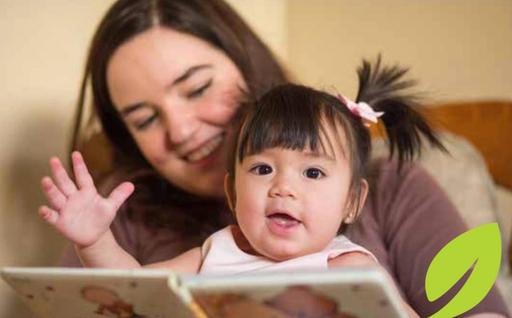 A woman reads a book with a little girl wearing pink braids in her pigtails