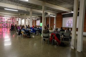 Group of people watching a presentation with a large sign reading 'Cecil Hotel' in the background