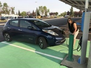 A smiling woman plugs her electric car into a charging booth