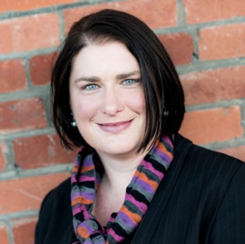 Headshot of woman wearing a scarf, against a brick backdrop