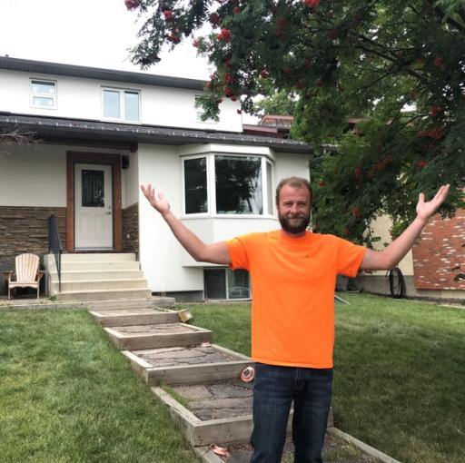 A man in an orange shirt raises his arms, showing off a net zero home.