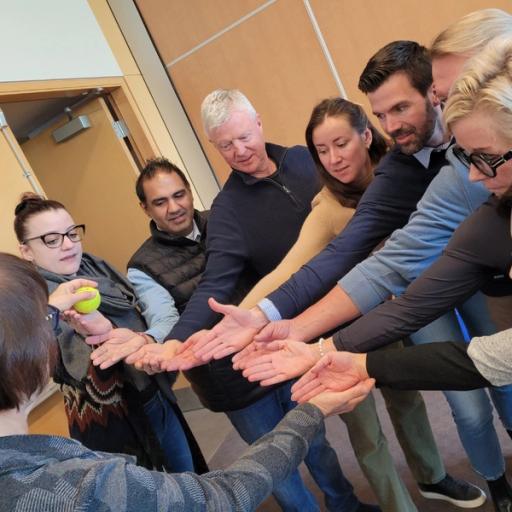 A group of team members participate in a team building exercise, letting a tennis ball roll down their hands