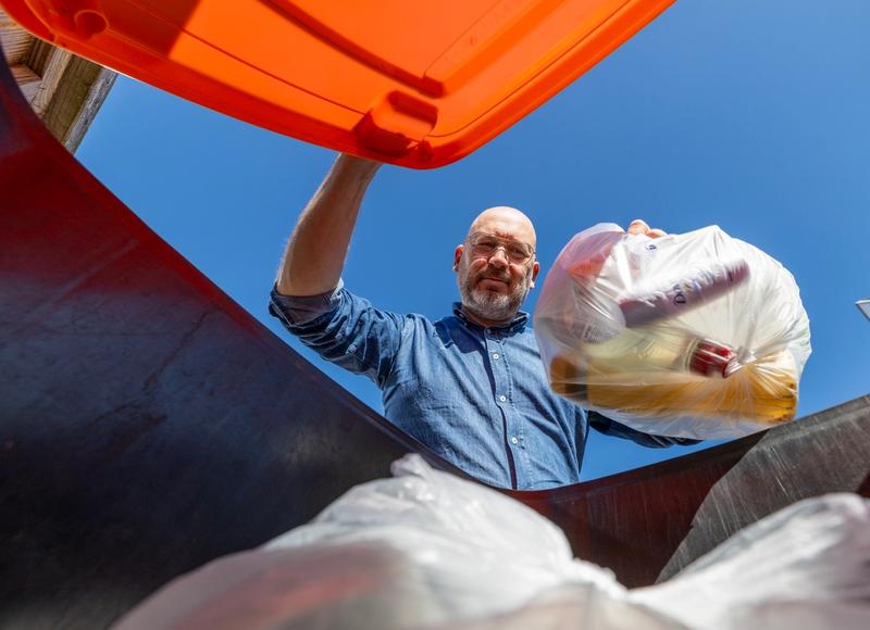 Inwoner gooit doorzichtige zak met afval in de verpakkingencontainer