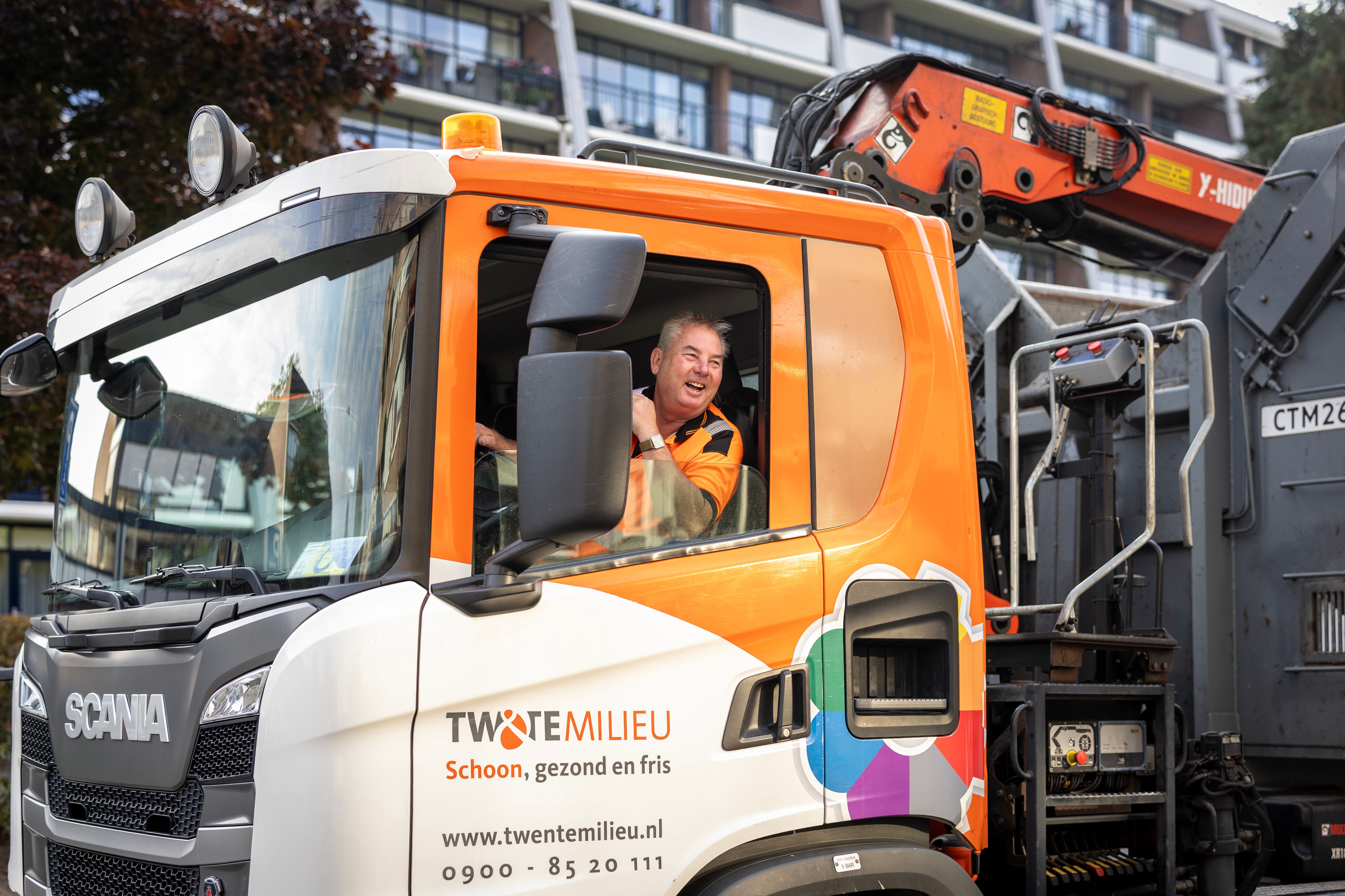Chauffeur vuilniswagen lacht door het raam heen