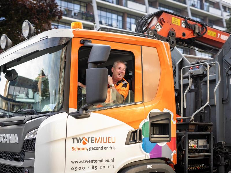 Chauffeur vuilniswagen lacht door het raam heen