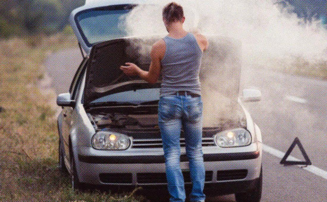A person standing in front of a smoking car with the hood up on the side of a road, signaling a breakdown.