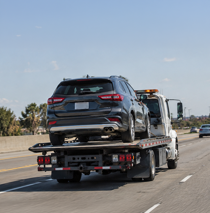 Damaged black car being towed away on a flatbed truck after being sold for cash