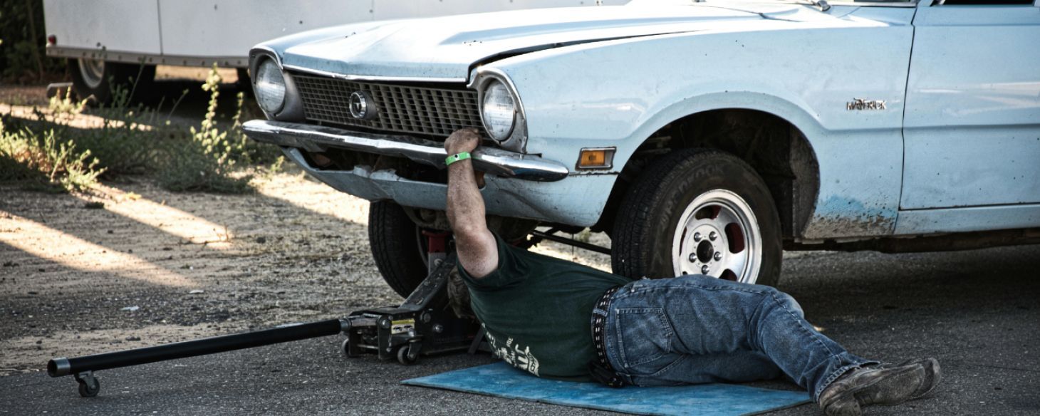 Man attaching a tow hook under a light blue vintage junk car before pickup