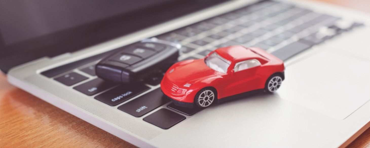 Red toy car and key fob on a laptop keyboard, representing selling a car online for cash