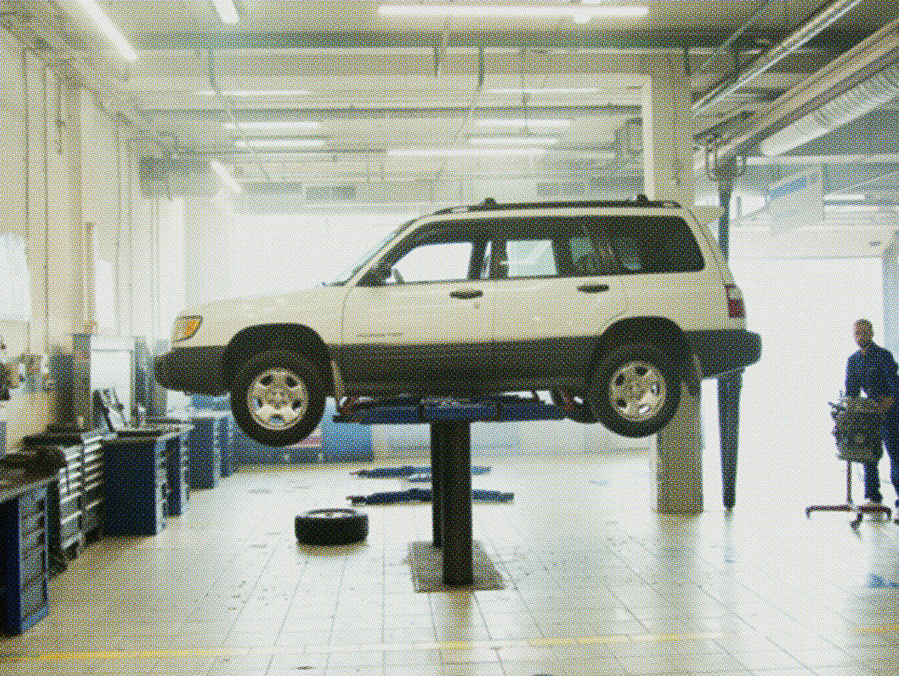 Old beige SUV raised on a hydraulic lift in an auto repair shop with a mechanic nearby, showing signs it needs costly car repairs