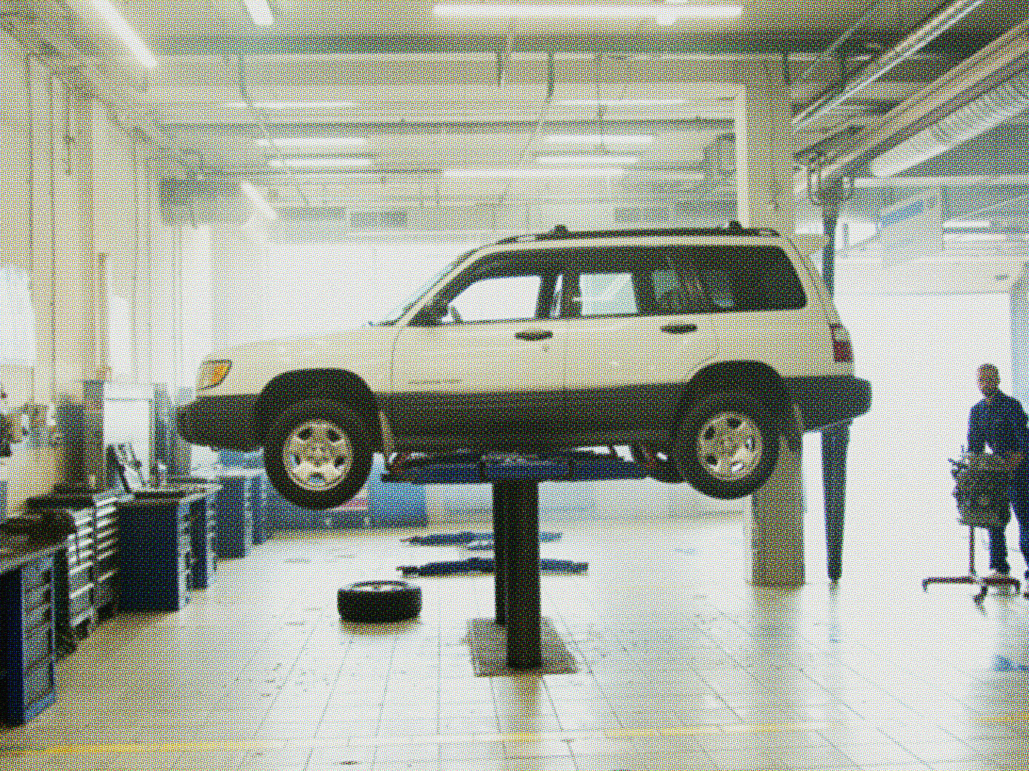 Old beige SUV raised on a hydraulic lift in an auto repair shop with a mechanic nearby, showing signs it needs costly car repairs