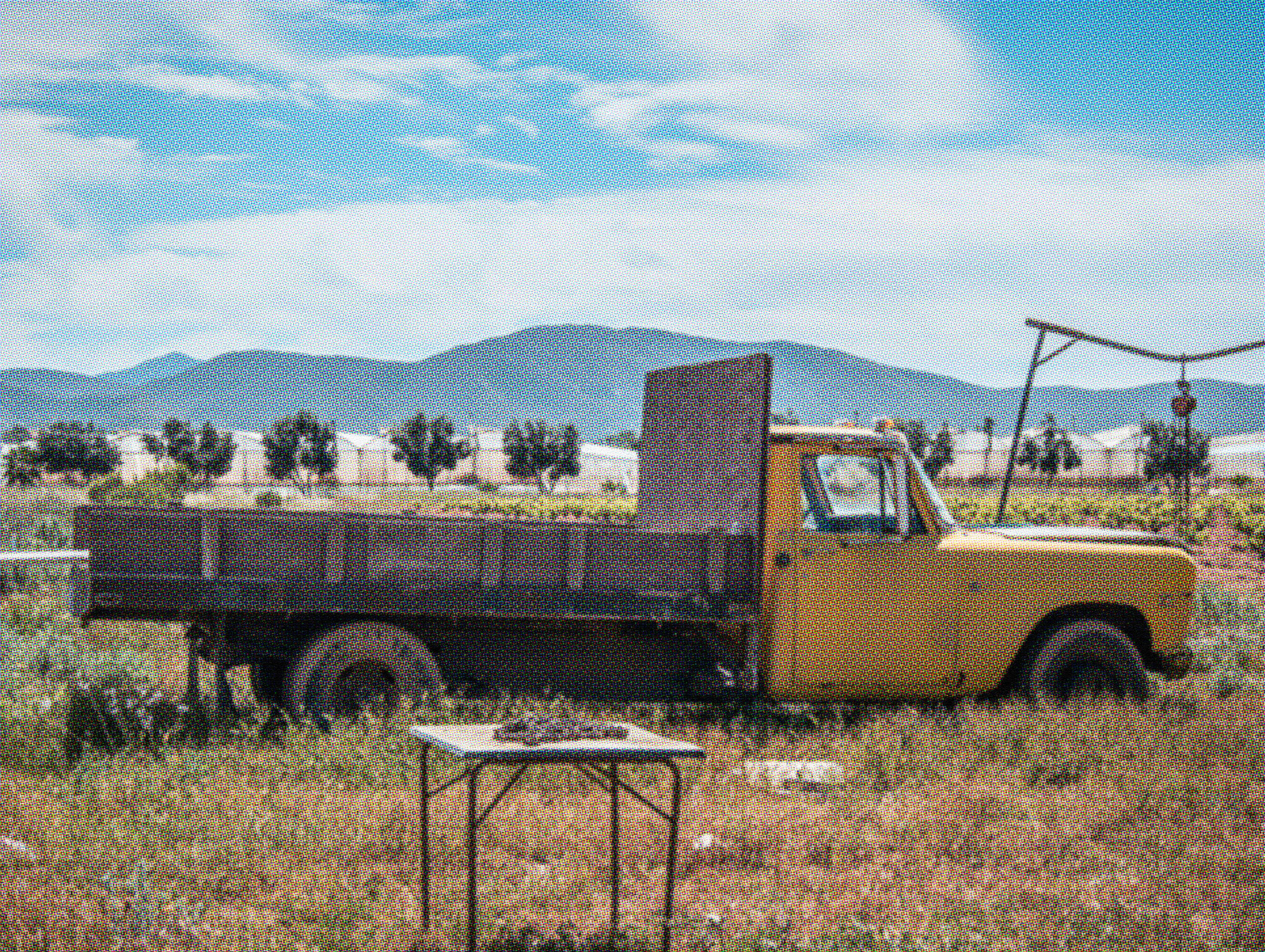 Vintage yellow flatbed work truck parked in a dry desert field with mountains in the background, showing signs of age and wear.