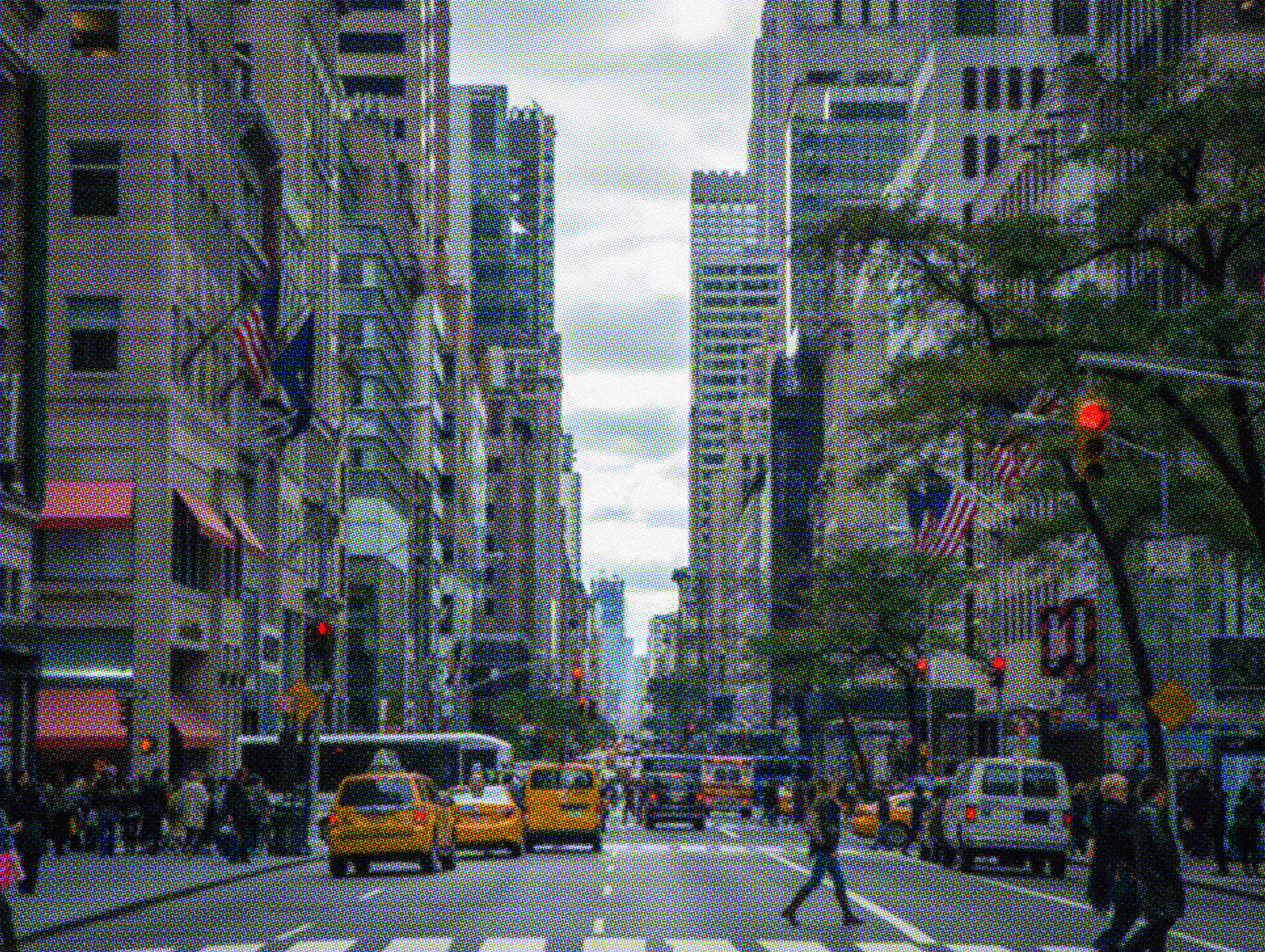 Busy big city street with yellow taxi cabs, pedestrians crossing, tall skyscrapers, and American flags lining a congested urban avenue.
