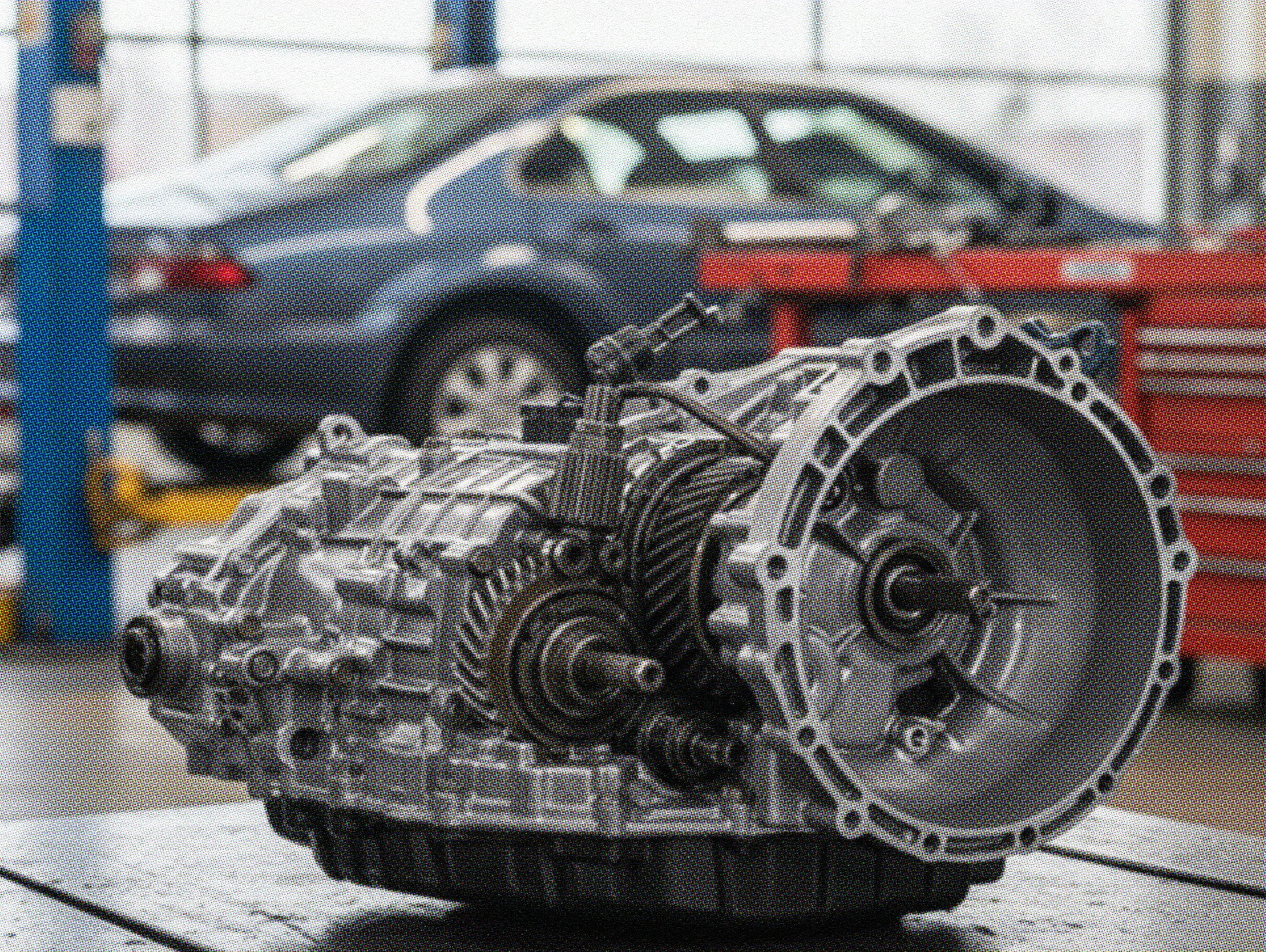 Close-up of a car transmission removed for repair in an auto shop, with a vehicle in the background—illustrating issues related to selling a car with a bad transmission.