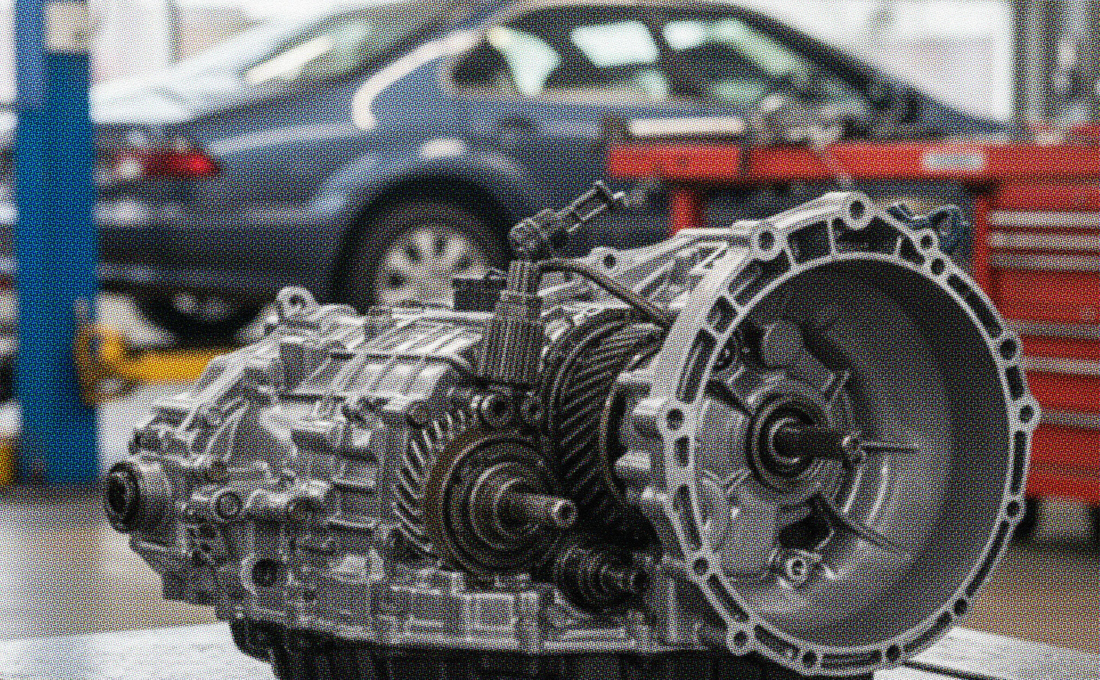 Close-up of a car transmission removed for repair in an auto shop, with a vehicle in the background—illustrating issues related to selling a car with a bad transmission.