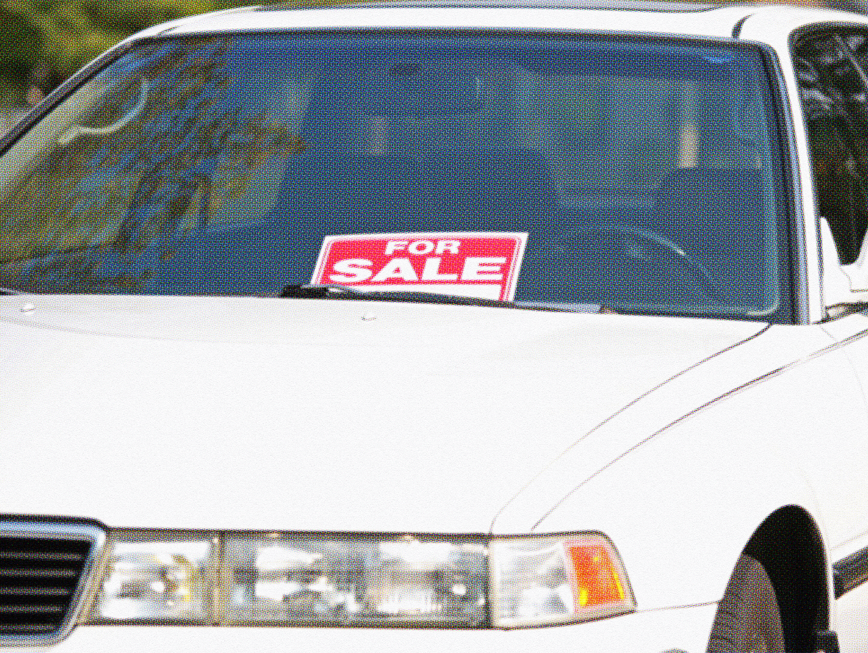 White sedan with a red "For Sale" sign displayed in the windshield, parked outdoors.