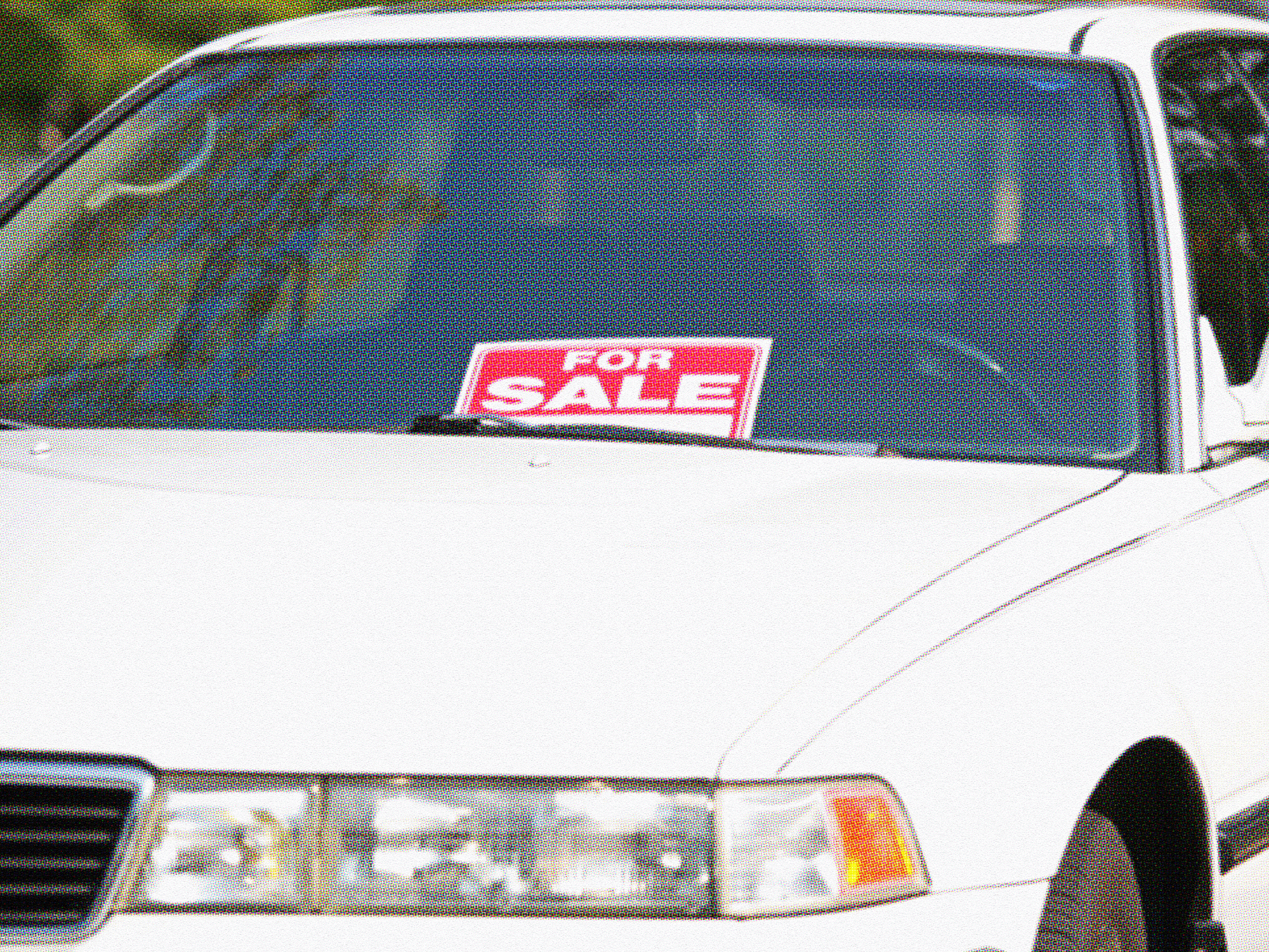 White sedan with a red "For Sale" sign displayed in the windshield, parked outdoors.