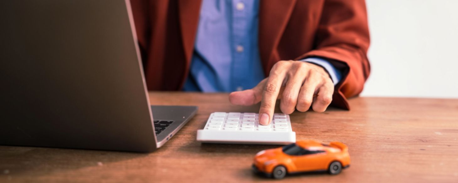 Man calculating used car value with calculator and laptop, toy car on desk representing vehicle valuation