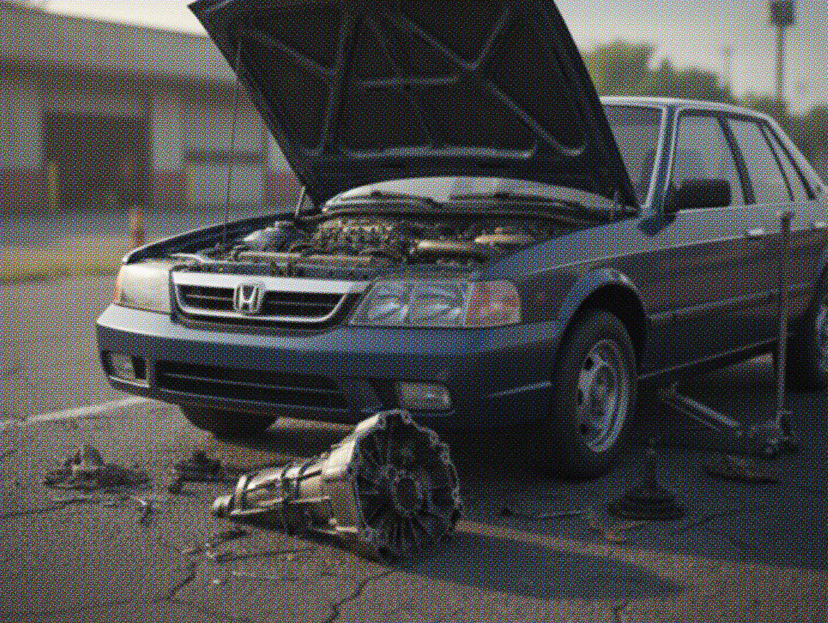 Older Honda sedan with the hood open and a blown transmission lying on the pavement, showing severe mechanical failure in a parking lot.