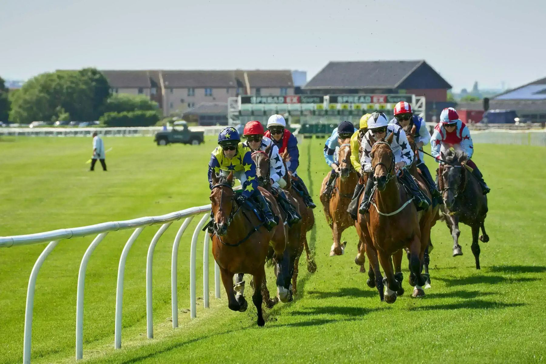 Jockeys racing thoroughbreds along the rail on a summer turf course.