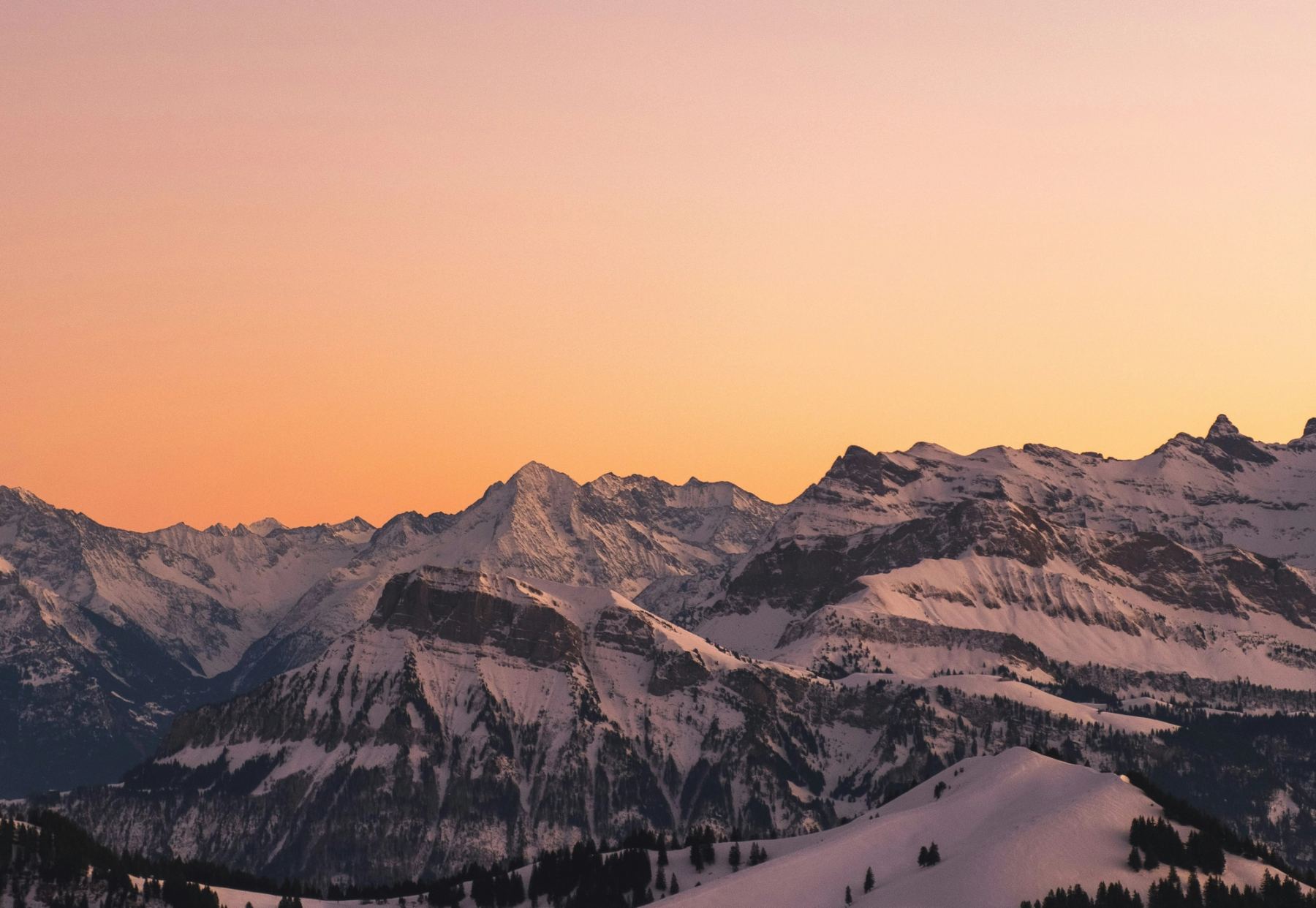 Snow-covered alpine peaks under a pink and orange sunset sky.