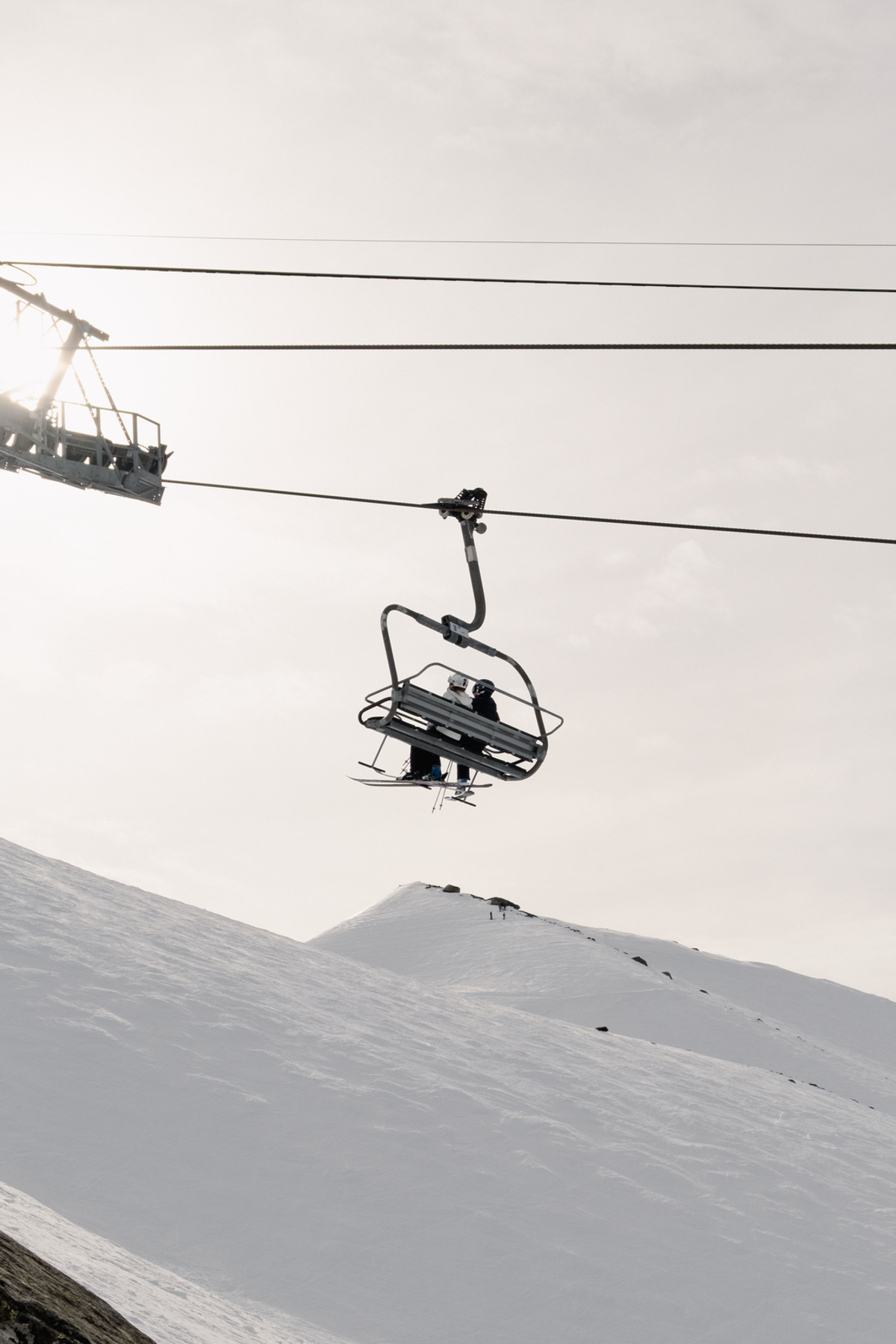 A chairlift carrying skiers hangs above a pale snowy ridge, with parallel cables crossing the upper part of the photograph.
