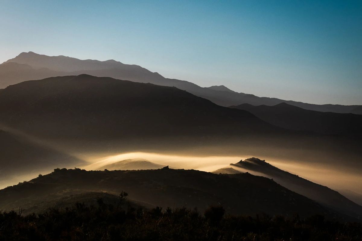 A luminous band of gold mist runs through the folds of a dark mountain landscape.