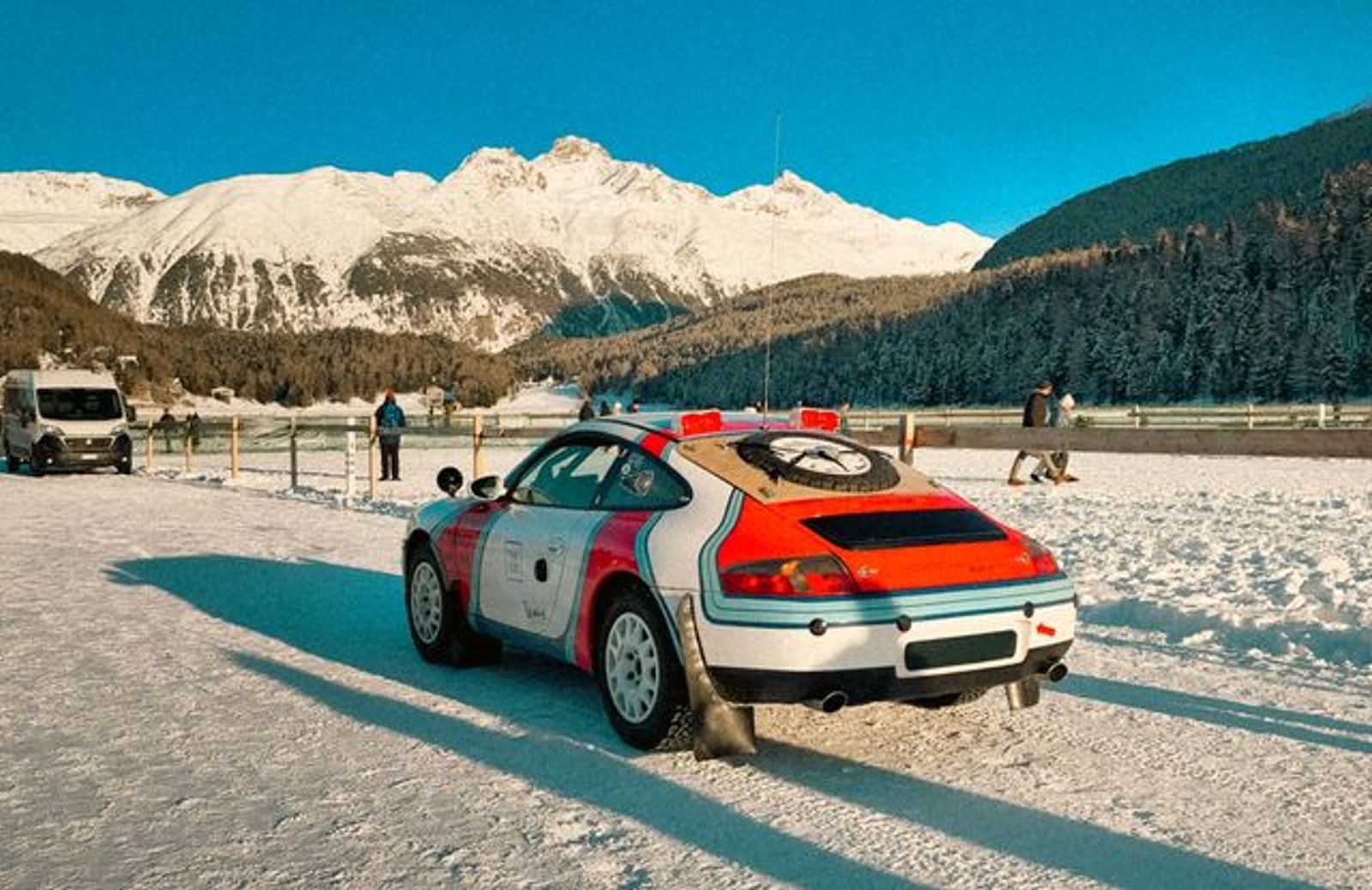Classic Porsche rally car on a snow-covered track with the Swiss Alps in the background.