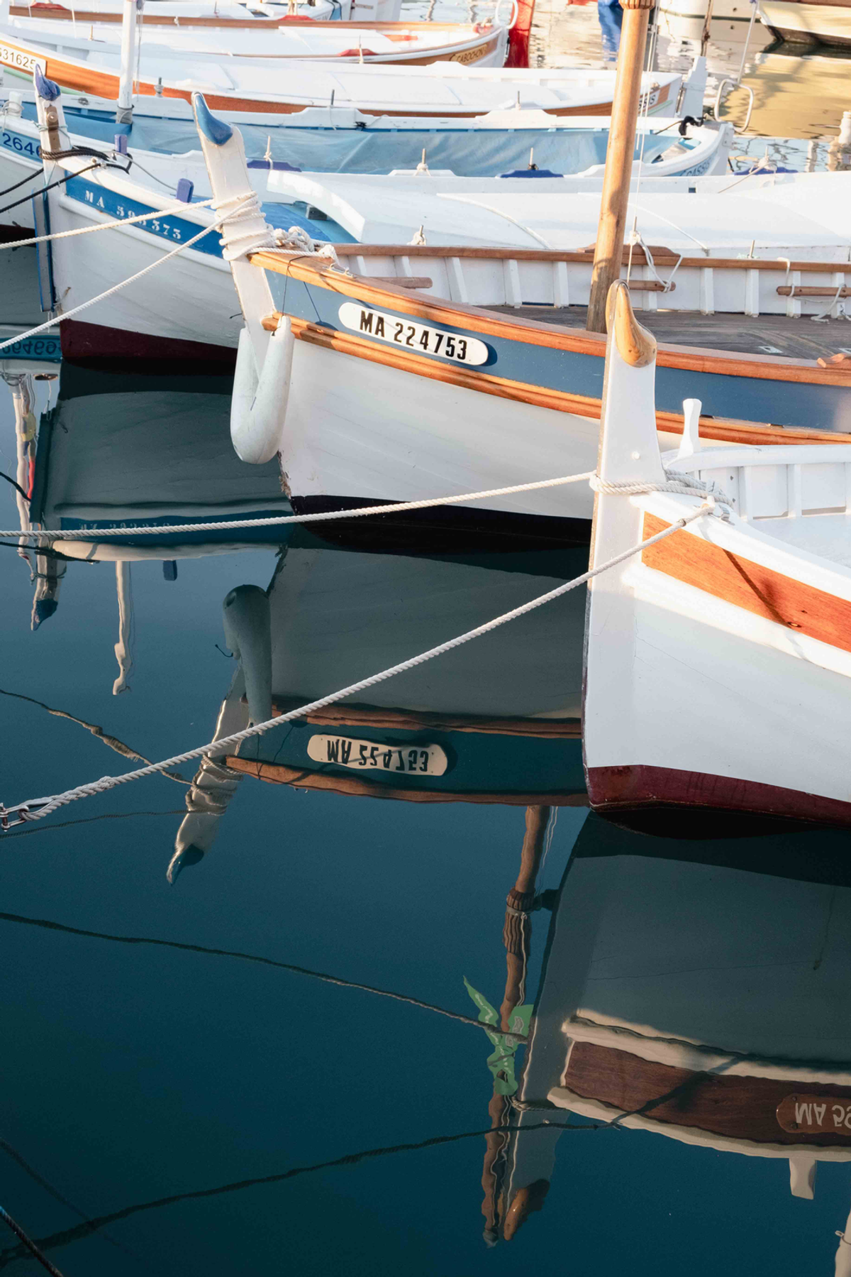 White hulls with wooden rails sit close together in a Côte d’Azur harbour, mooring ropes crossing dark teal water.