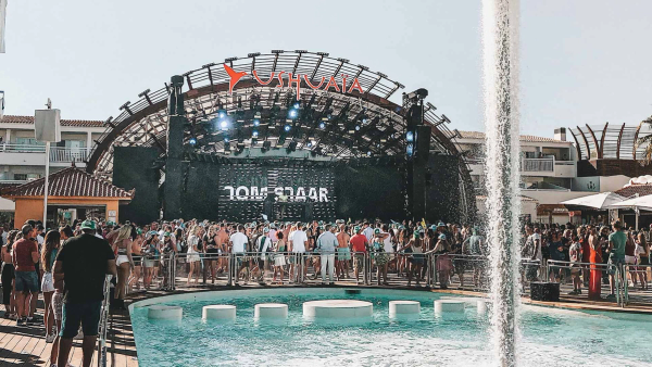 The open-air stage at Ushuaïa Ibiza under its arched rig, with the crowd gathered around the pool in daylight.