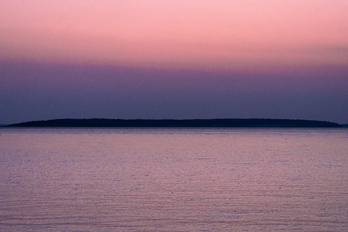 Pink light settles across open water, with a low strip of land holding the horizon.