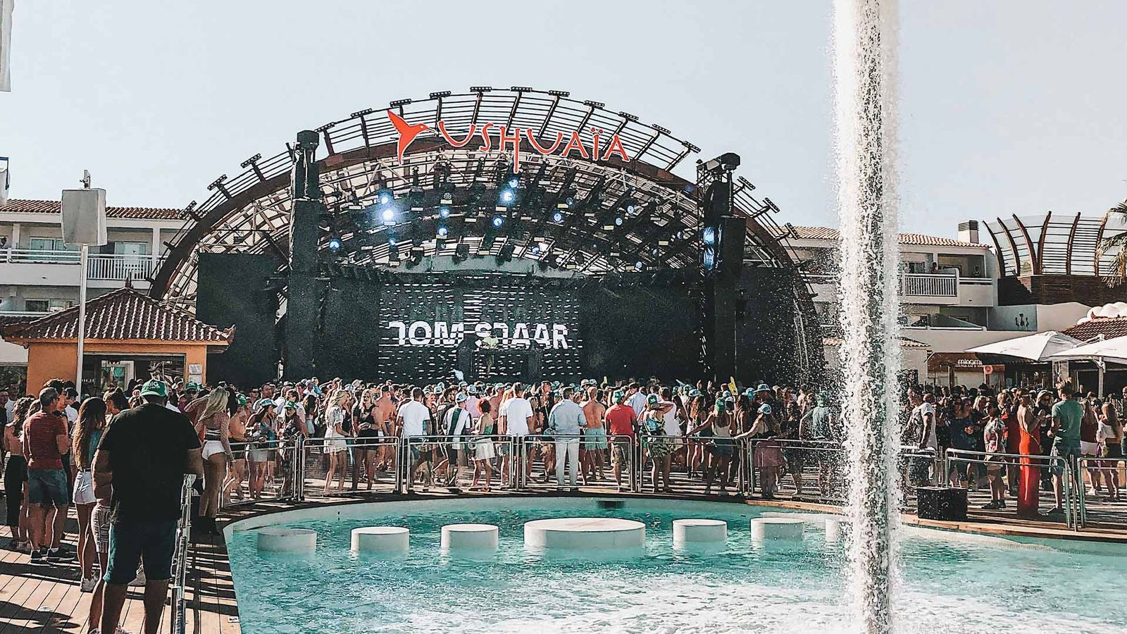 Daytime pool party at Ushuaïa Ibiza: crowd before the open-air stage as a fountain rises over the pool.