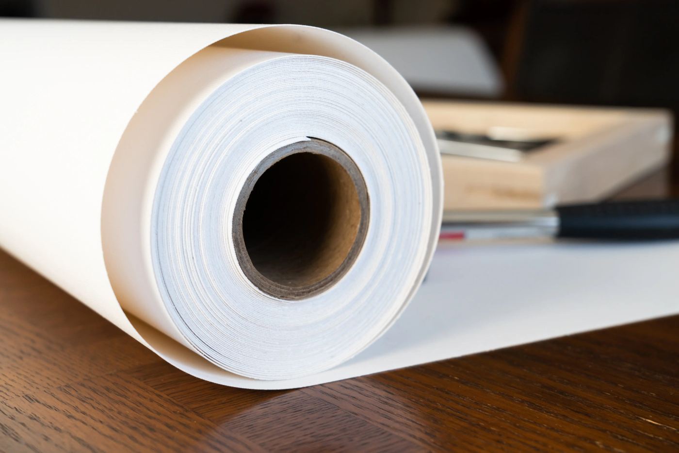 Roll of fine-art print paper on a wooden desk beside framing tools.