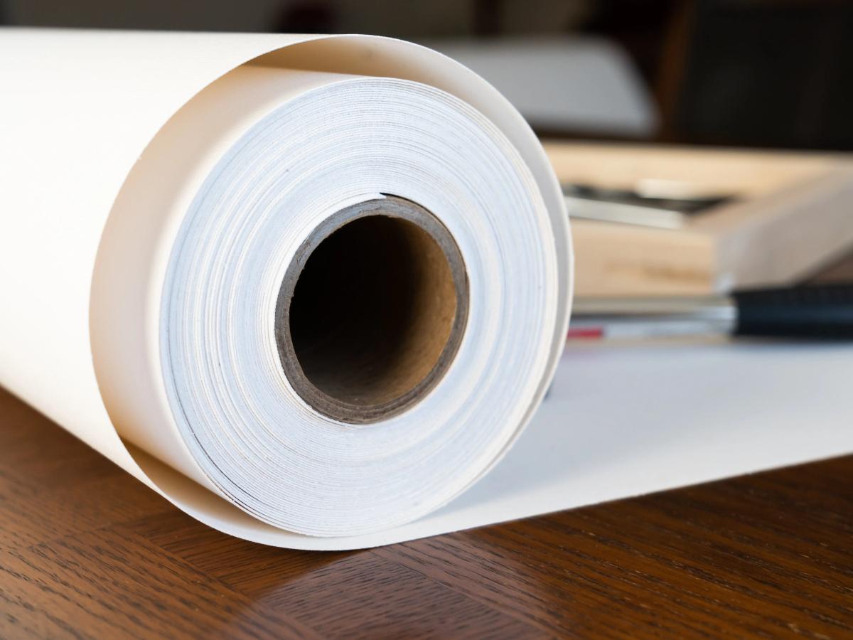 Roll of fine-art print paper on a wooden desk beside framing tools.