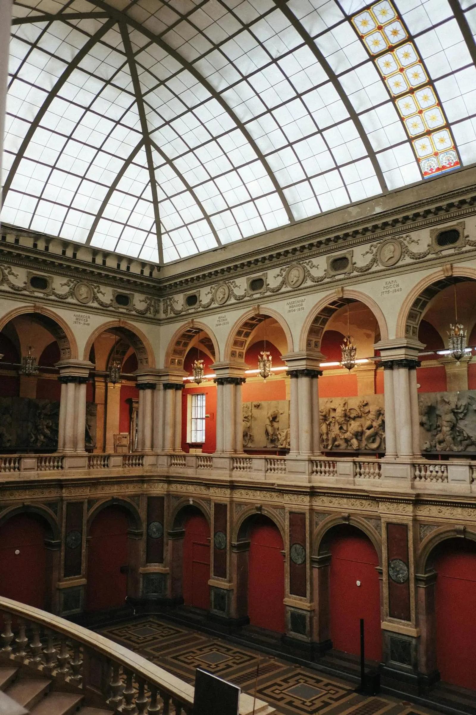 Neoclassical museum atrium with a vaulted glass ceiling, red walls, and stone archways