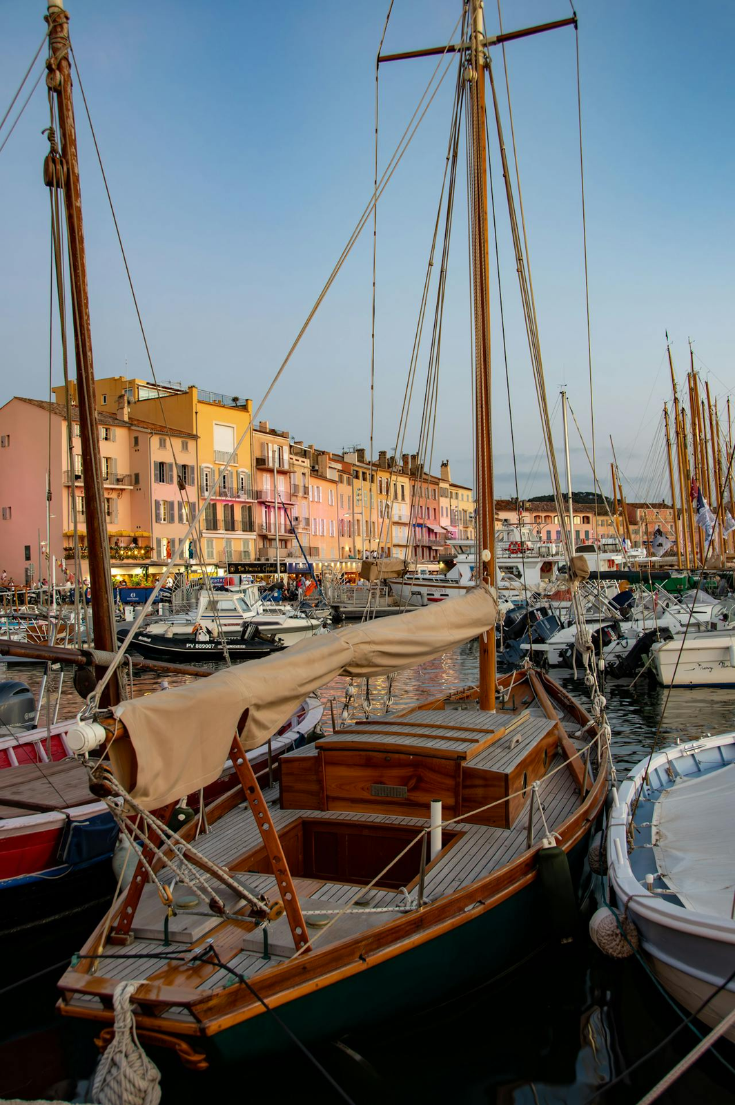 Classic wooden sailing boat moored in St Tropez harbour with colourful Mediterranean buildings