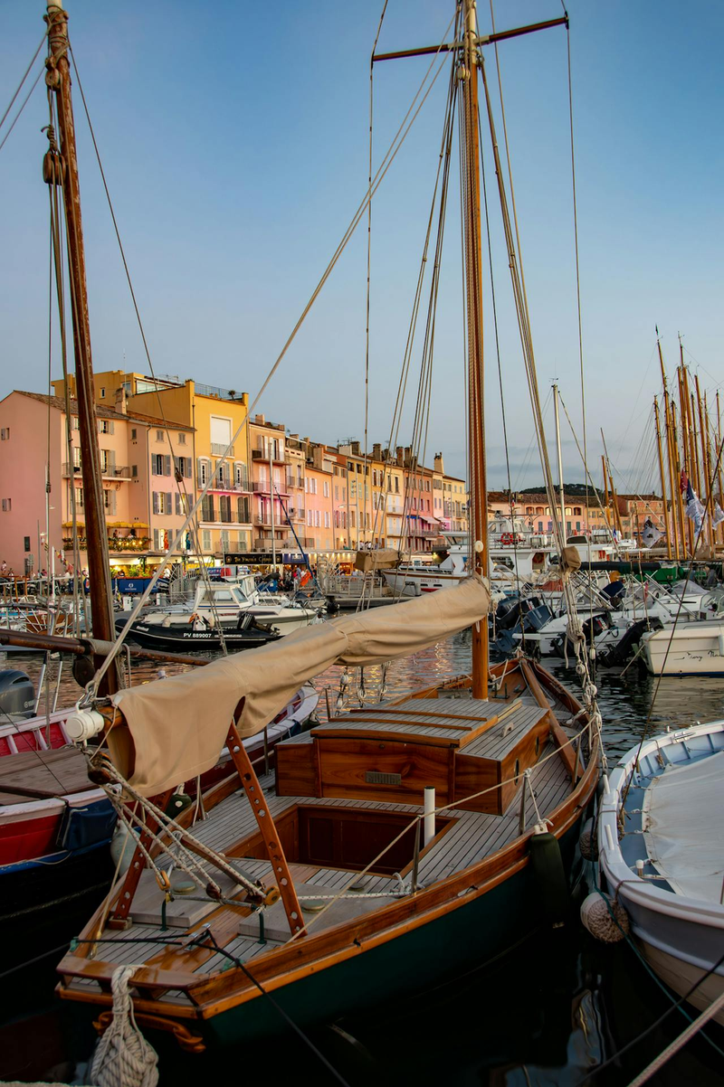 Classic wooden sailing boat moored in St Tropez harbour with colourful Mediterranean buildings