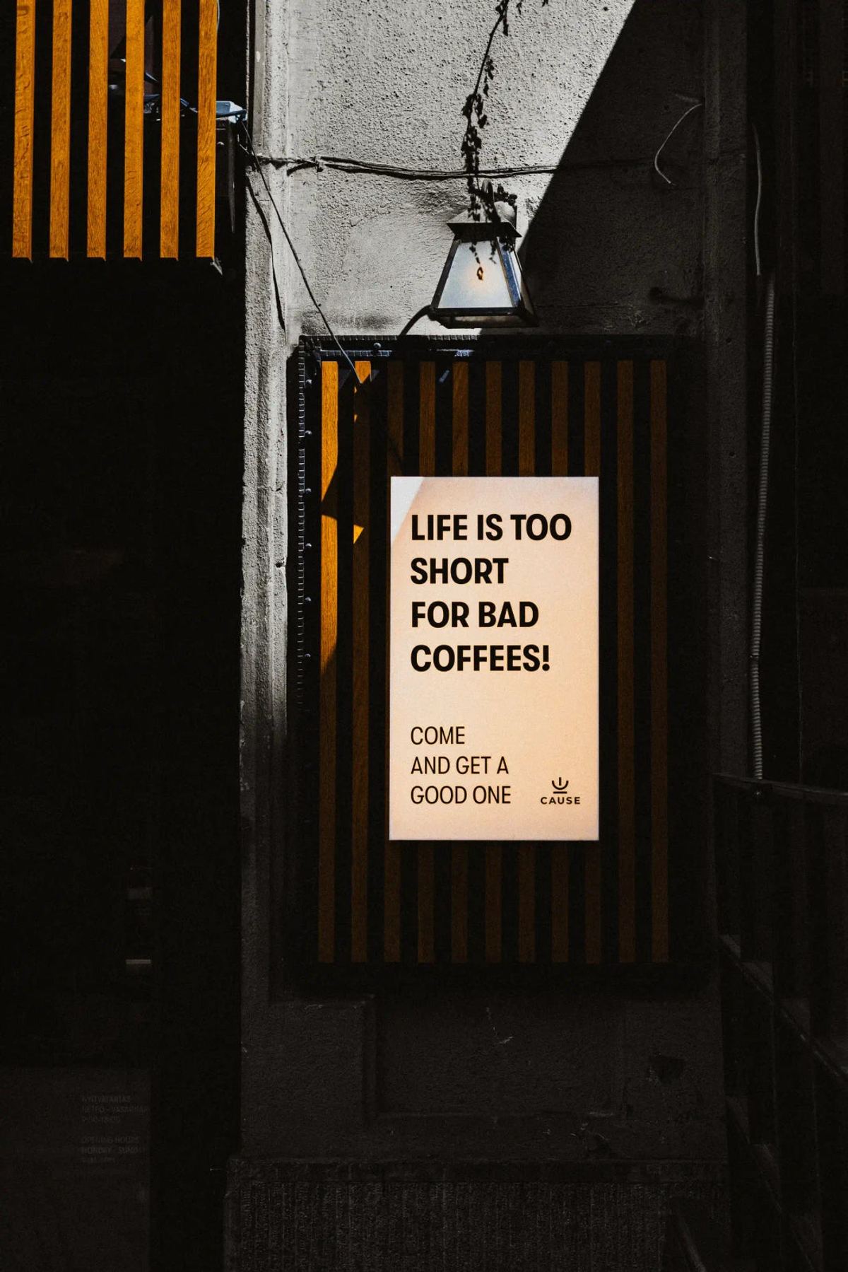 Cream cafe sign reading 'Life is too short for bad coffees!' against dark wooden slats beneath a hanging lamp.