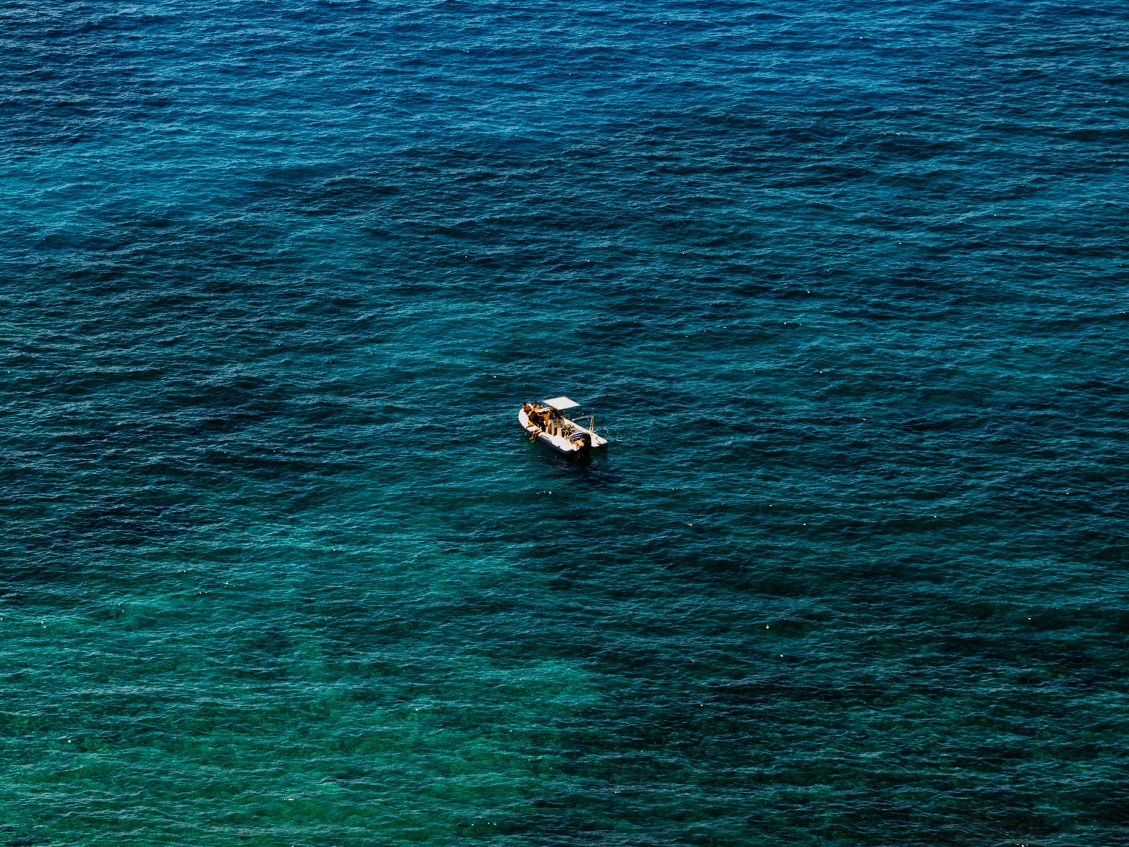 Small white boat alone on deep blue-green open water, seen from above.