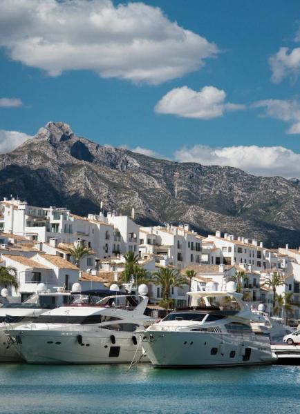 Luxury white yachts moored in a Spanish marina with whitewashed buildings and mountains behind