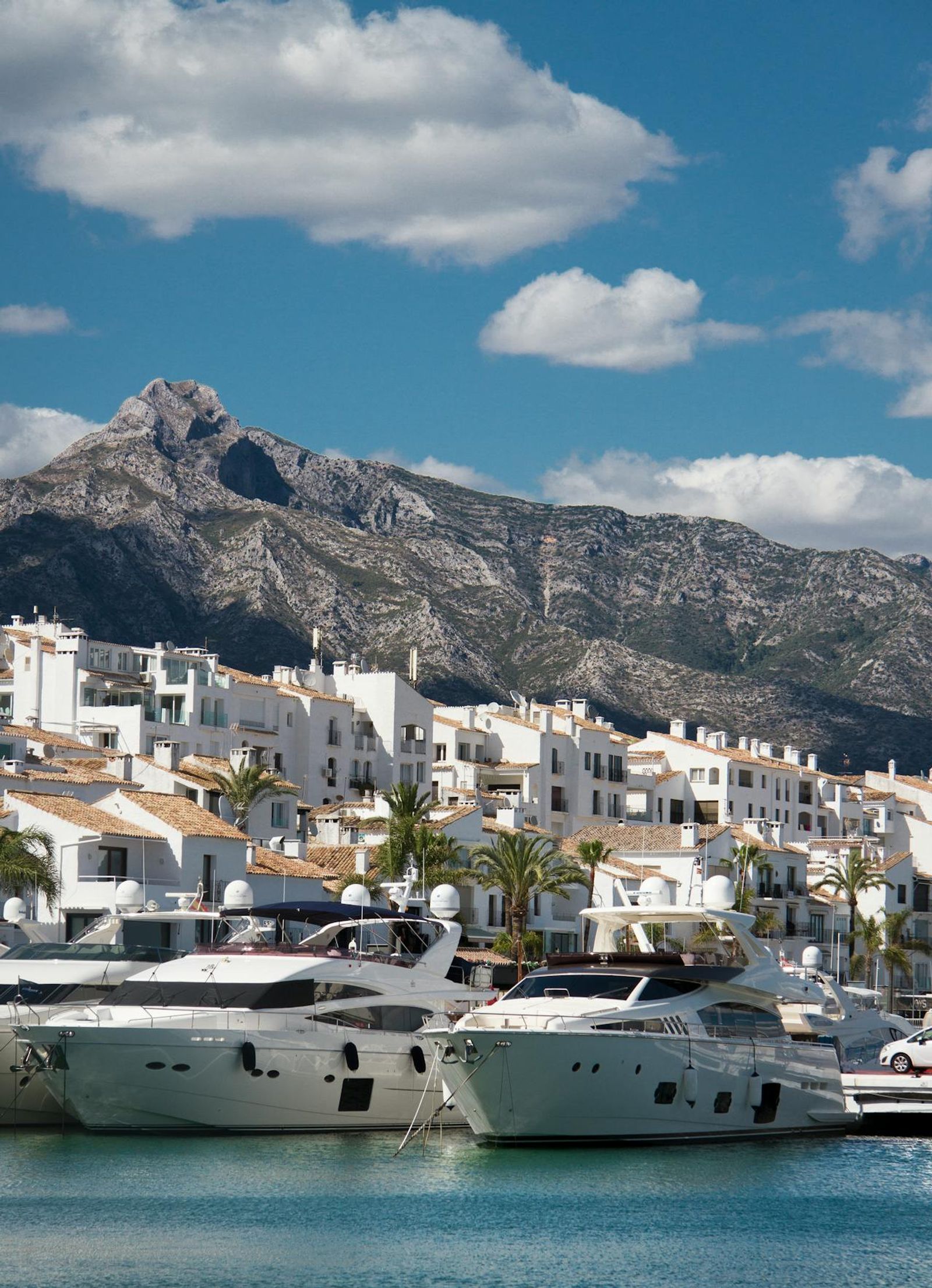 Luxury white yachts moored in a Spanish marina with whitewashed buildings and mountains behind