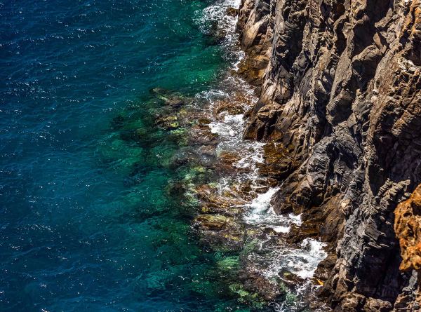 Rugged cliff face meeting clear turquoise water, seen from above.