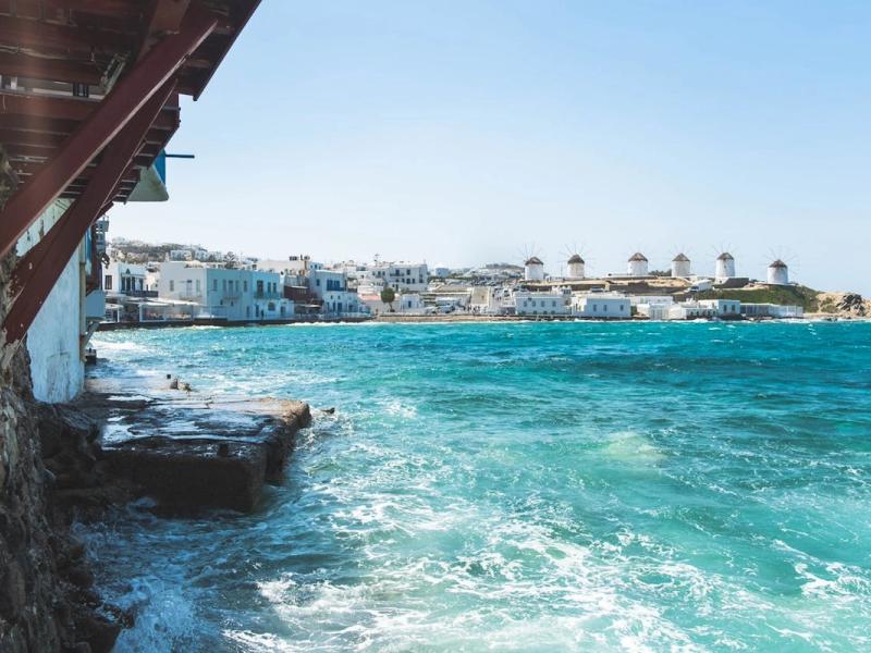 Rugged coastline of Mykonos featuring the iconic white windmills on the horizon