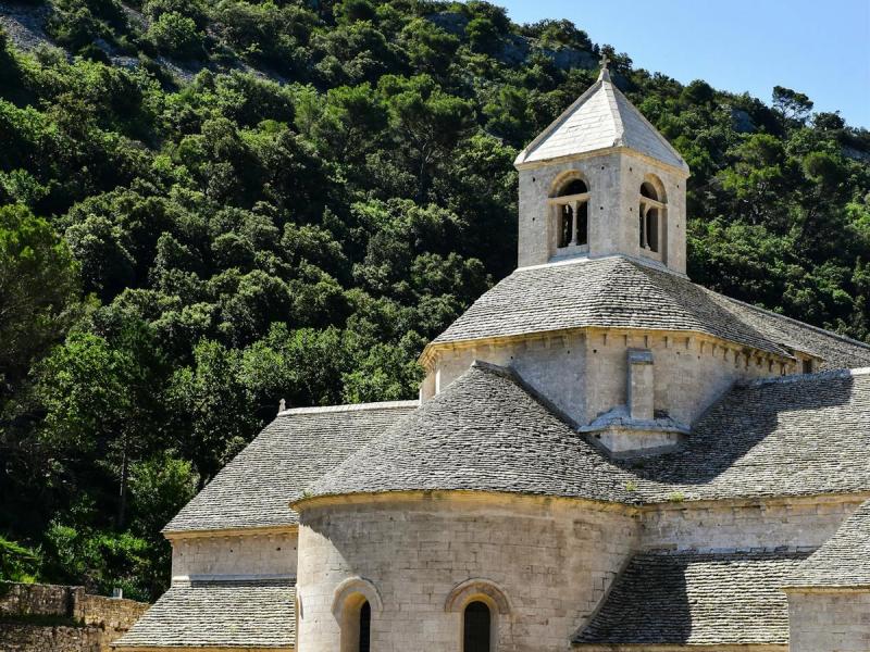 Sénanque Abbey in Provence with blooming lavender fields and forested hills under a blue sky